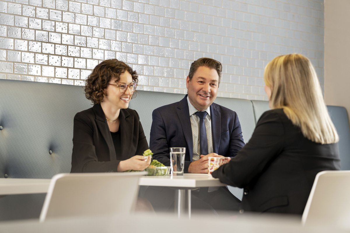 An Associate lawyer is being mentored by two partners at Bishop & McKenzie in a café setting