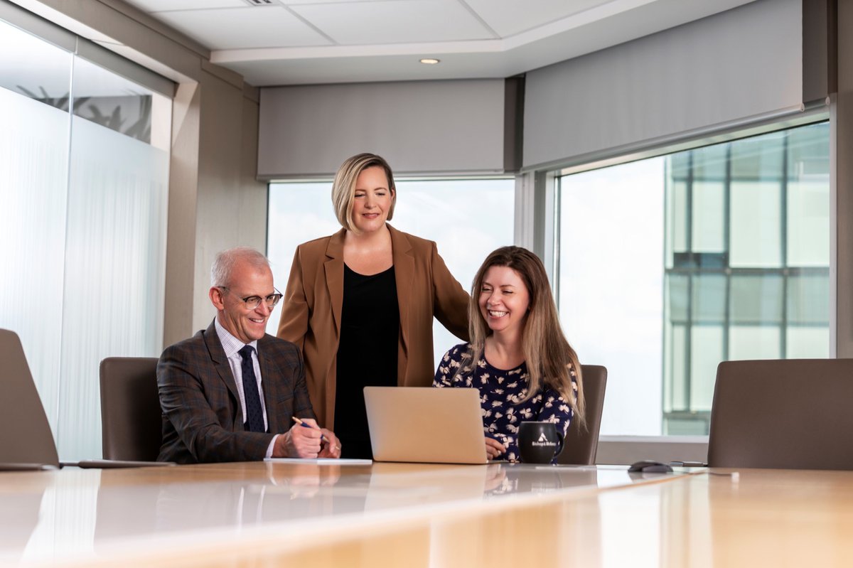 Three senior lawyers (1 male, 2 female) gather around a laptop in the boardroom, putting the final touches on a client file.